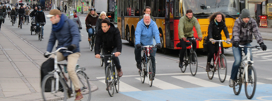 Tæt strøm af cyklister på vej ud i et gadekryds i bymæssige omgivelser