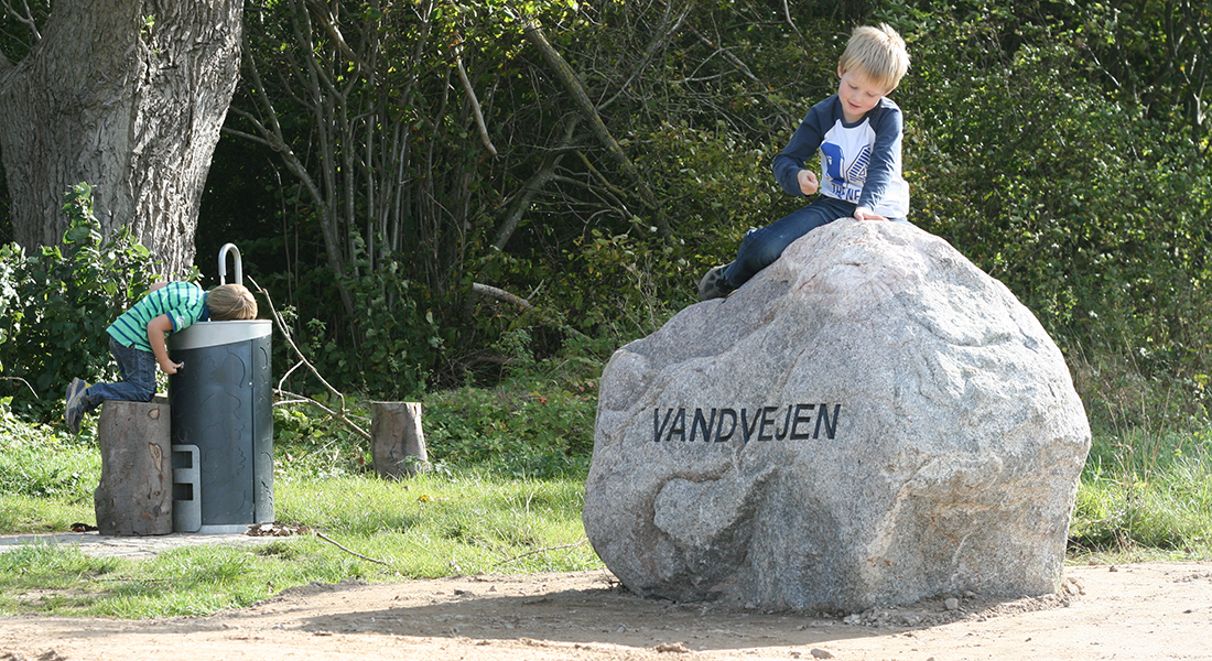 Et mindre barn på toppen af stor sten og et andet ved en vandpost